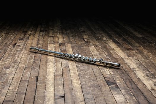 silver metal flute lies on a wooden stage in the dark