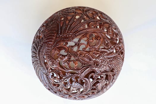 Close up ornamental shell for candle. Carved Souvenir from Coconut. Traditional handicraft on Bali, Indonesia. Hand carved ornaments with animal and plant motifs on the coconut shell. Mystical dragon.