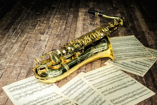 shiny golden saxophone lies near sheet music letters on a wooden stage