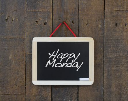 Blackboard hanging on a old wooden wall with phrase Happy Monday.