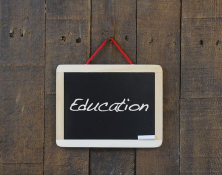 Blackboard hanging on a old wooden wall with word Education.