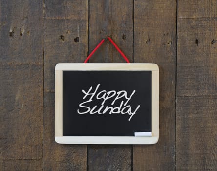 Blackboard hanging on a old wooden wall with phrase Happy Sunday.