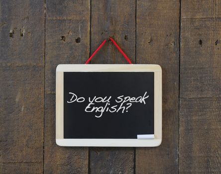 Blackboard hanging on a old wooden wall with phrase do you speak english.