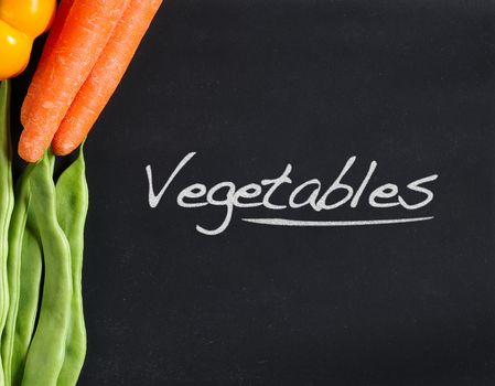 Fresh vegetables as carrots, beans and peppers on a blackboard.