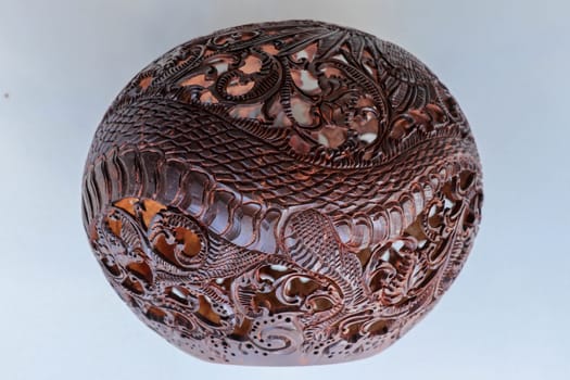 Close up ornamental shell for candle. Carved Souvenir from Coconut. Traditional handicraft on Bali, Indonesia. Hand carved ornaments with animal and plant motifs on the coconut shell. Mystical dragon.