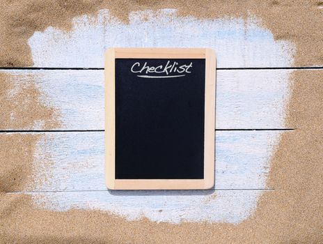 Blackboard and blue wooden table on beach sand.