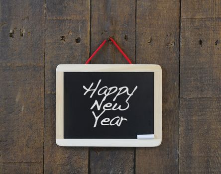 Blackboard hanging on a old wooden wall with Happy New Year.