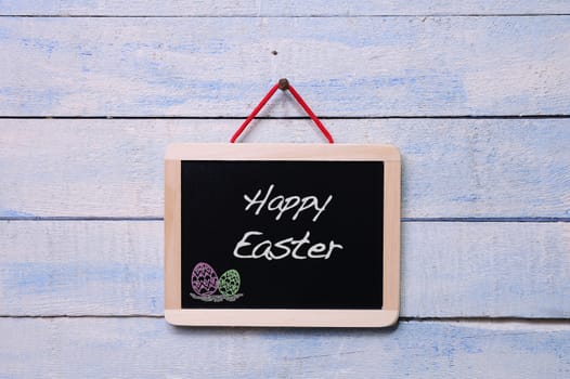 Blackboard hanging on a old wooden wall with word Happy Easter.