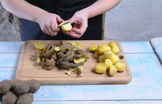 Peeling potatoes on wooden table in the kitchen.