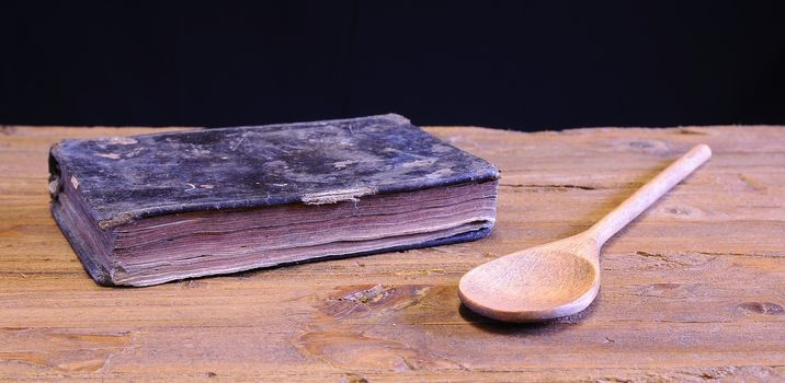 Old cookbook on wooden table with a wooden spoon