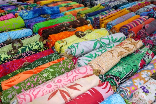 Rolled up colored fabrics tied with string. Shop with brightly colored sarongs. Sarung pantai ready for sale on Bali island. Part of traditional Hindu clothing of believers on Bali island. Background.