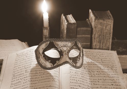 Carnival mask over an old book in the light of a candle.