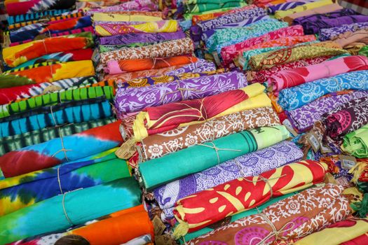 Rolled up colored fabrics tied with string. Shop with brightly colored sarongs. Sarung pantai ready for sale on Bali island. Part of traditional Hindu clothing of believers on Bali island. Background.