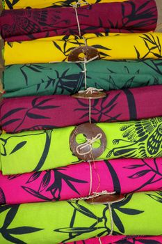 Rolled up colored fabrics tied with string. Shop with brightly colored sarongs. Sarung pantai ready for sale on Bali island. Part of traditional Hindu clothing of believers on Bali island. Background.