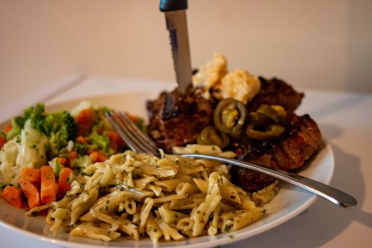 Close up view of a plate of tenderloin steak,medium rare, served with pasta and vegetable on white background.