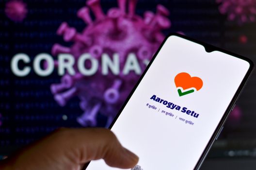 New Delhi, India, 2020. Aarogya Setu app, developed by government of India to track the Covid-19 status, Logged in on a mobile infront of a screen showing microscopic 3D illustration of Corona Virus