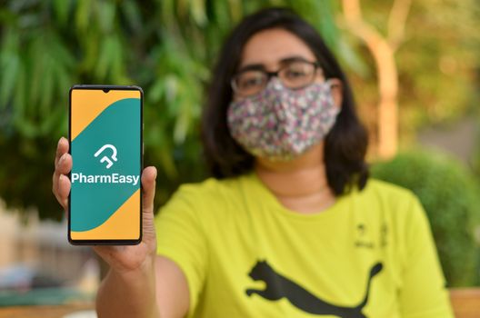 New Delhi, India, 2020. Girl wearing mask with Pharmeasy app on the mobile phone. Only essential services / products are allowed to be delivered during Corona Virus (Covid-19) lockdown