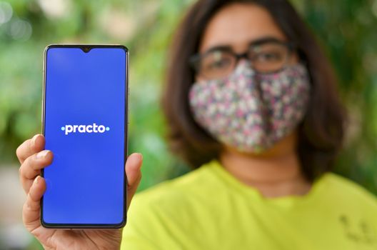 New Delhi, India, 2020. Girl wearing mask with Practo app on the mobile phone. Only essential services / products are allowed to be delivered during Corona Virus (Covid-19) lockdown