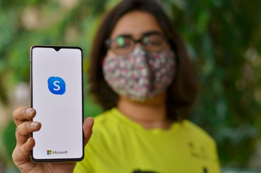 New York, USA,2020. Girl wearing mask show Skype app on mobile under home quarantine for Corona virus (Covid-19) disease pandemic.Skype has become most popular video conferencing app during lockdown