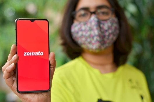 Mumbai, India, 2020. Girl wearing mask showing Zomato Food Delivery app on a mobile phone. During Corona Virus (Covid-19) disease pandemic lock down, delivery of food and essential service is allowed