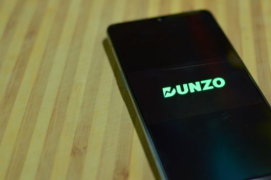 New Delhi, India, 2020. Flat lay Dunzo Delivery app logo glowing on the mobile phone screen on a wooden background. Selective focus and shallow depth of field. The main focus is on the logo.