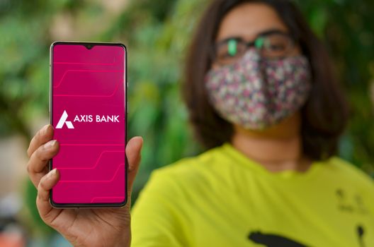 New Delhi, India, 2020. Girl wearing a face mask showing Axis bank app during Corona Virus (Covid-19) disease pandemic. People are encouraged to not visit the bank but do digital banking transactions