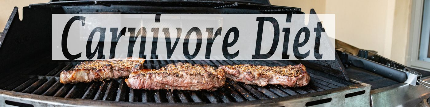 The word Carnivore diet on a panorama of a barbeque with steaks on it. Concept of the controversial diet.