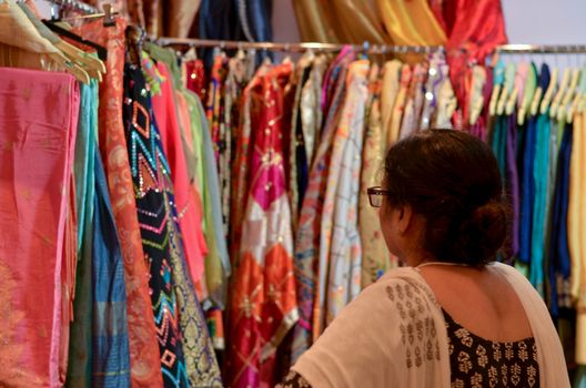 A senior Indian woman wearing glasses checking designer kurta ( Salwar Kamiz) on display at a shop in Dilli Haat or Sarojini nagar market in New Delhi, India