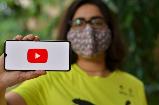 Delhi, India,2020. Girl wearing mask show Youtube app on mobile under home quarantine for Corona virus (Covid-19) disease pandemic. Youtube is very population app among all the generations