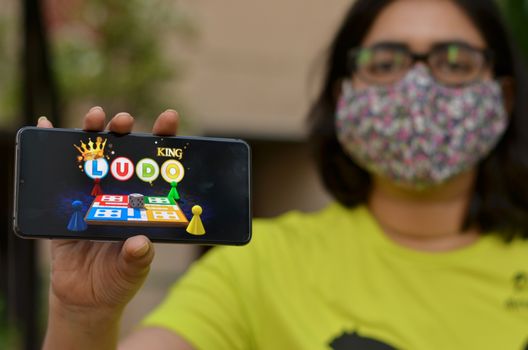 New Delhi, India, 2020. Girl wearing surgical face mask showing Ludo King game app on her mobile phone screen. Due to Corona Virus (covid-19) disease pandemic lock down, the users play these games