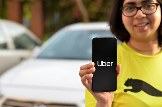 New Delhi, India, 2020. Girl showing Uber app on her mobile phone screen while standing in front of her fleet of cars. Its an aggregator service for booking taxi cabs ride. Concept On the go