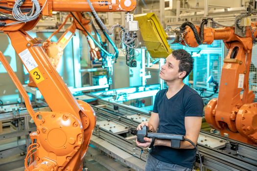 engineer controls using remote control of industrial robot in factory. Automatic welding and gluing using automation and robotic arms.