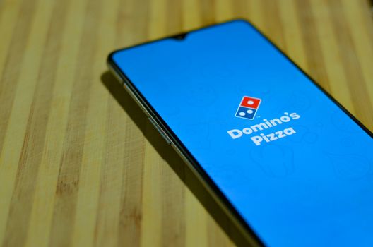 New Delhi, India, 2020. Flat lay mobile phone showing Domino's pizza delivery mobile app during on a wooden board background. Delivery of food is allowed during Corona Virus Disease (Covid-19)