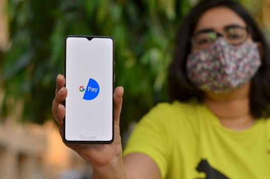 New Delhi, India, 2020. Girl wearing a face mask showing Google Pay app during Corona Virus (Covid-19) disease pandemic. People are encouraged to not use case but do digital banking transactions