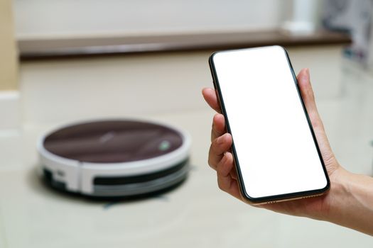 Hand holding smartphone with blanking screen for control robotic vacuum cleaner . Smart life technology concepts.