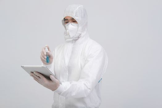 man scientist wearing biological protective uniform suit clothing, mask, gloves spraying sanitizer on tablet for sanitizing virus bacteria