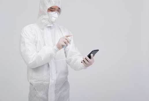 man scientist wearing biological protective uniform suit clothing, mask, gloves spraying sanitizer on smartphone for sanitizing virus bacteria