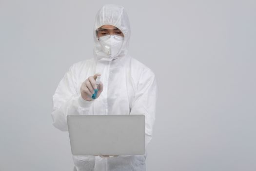 man scientist wearing biological protective uniform suit clothing, mask, gloves spraying sanitizer on computer for sanitizing virus bacteria
