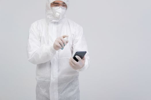 man scientist wearing biological protective uniform suit clothing, mask, gloves spraying sanitizer on smartphone for sanitizing virus bacteria