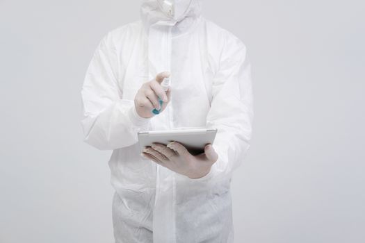 man scientist wearing biological protective uniform suit clothing, mask, gloves spraying sanitizer on tablet for sanitizing virus bacteria