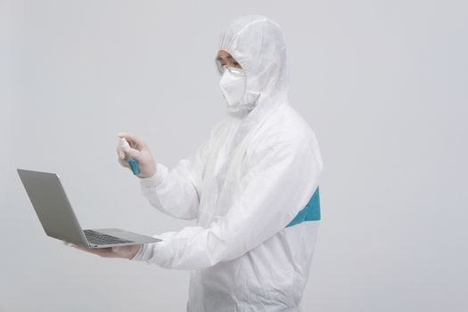 man scientist wearing biological protective uniform suit clothing, mask, gloves spraying sanitizer on computer for sanitizing virus bacteria