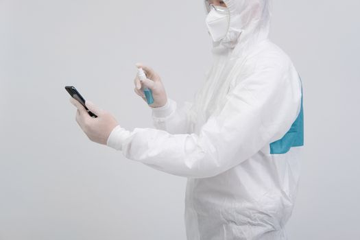 man scientist wearing biological protective uniform suit clothing, mask, gloves spraying sanitizer on smartphone for sanitizing virus bacteria