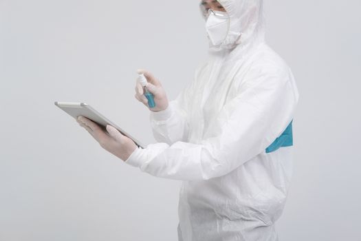 man scientist wearing biological protective uniform suit clothing, mask, gloves spraying sanitizer on tablet for sanitizing virus bacteria