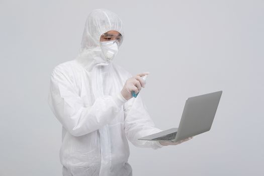 man scientist wearing biological protective uniform suit clothing, mask, gloves spraying sanitizer on computer for sanitizing virus bacteria
