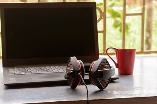 Portable over-ear Binaural Sound USB Headset with Microphone Noise Cancelling and Ultrasonic Volume Adjuster Headphone for Computer, Skype placed near laptop on window sunlight in morning. Red Cup of Coffee at a distance. Stay home, Work from home, Remote Work, Business Continuity background.