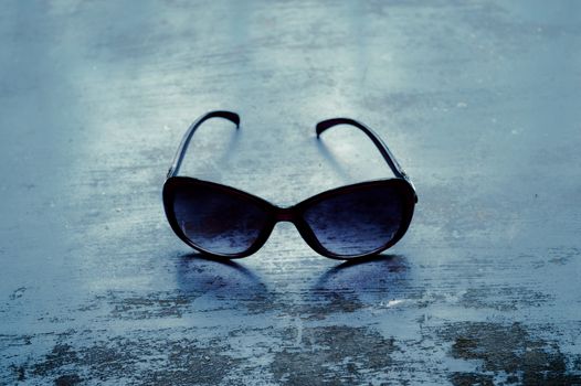 Blue modern fashionable Sunglasses on rustic floor. Fashion background. Still life photography. Sunlight reflection from back. Lens shadow on floor.