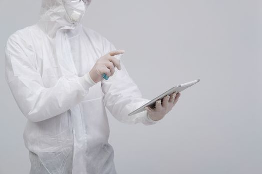 man scientist wearing biological protective uniform suit clothing, mask, gloves spraying sanitizer on tablet for sanitizing virus bacteria