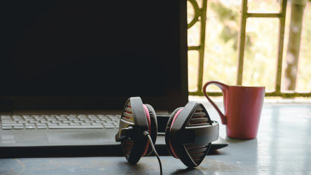 Portable over-ear Binaural Sound USB Headset with Microphone Noise Cancelling and Ultrasonic Volume Adjuster Headphone for Computer, Skype placed near laptop on window sunlight in morning. Red Cup of Coffee at a distance. Stay home, Work from home, Remote Work, Business Continuity background.