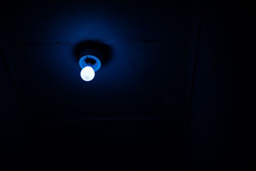 Blue light bulb shining from ceiling of room
