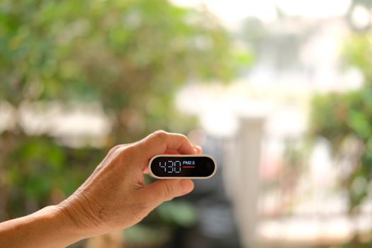 people hand holding pm 2.5 detector for checking air quality. air pollution from fine particle causing bad unhealthy weather